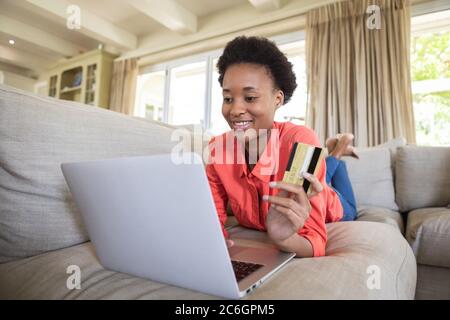 Frau mit Kreditkarte mit Laptop, während sie auf der Couch lag Stockfoto