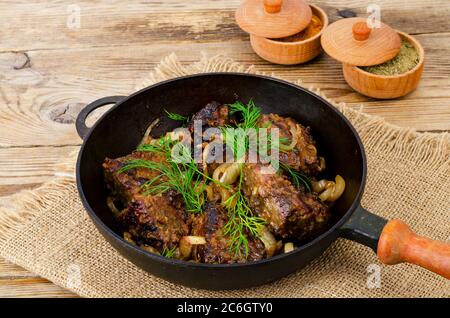 Gusseiserne Bratpfanne auf Holztisch mit gebratener Leber. Stockfoto