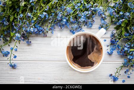 Blaue Vergiss-mich-nicht Blumen und eine Tasse heißen Kaffee auf einem weißen Holztisch Stockfoto