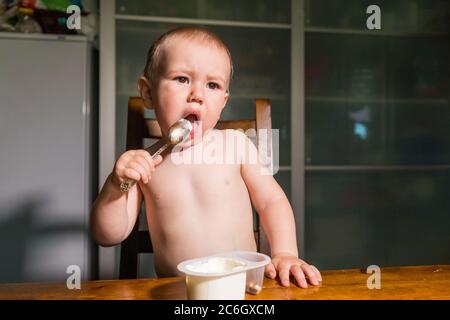 Liebenswert Baby Junge essen Hüttenkäse aus Löffel, gesunde Milch Snack. Stockfoto