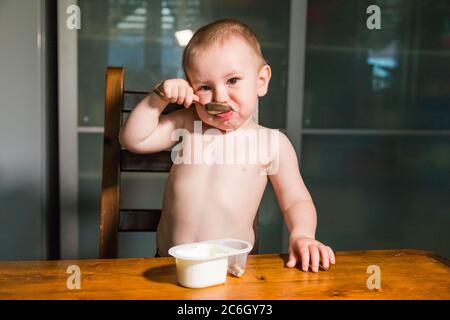 Liebenswert Baby Junge essen Hüttenkäse aus Löffel, gesunde Milch Snack. Stockfoto