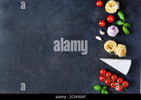 Italienische Pasta Zutaten zum Kochen. Rohe Pasta, Gemüse, Gewürze und Kräuter Draufsicht auf schwarzem Hintergrund. Italienische gesunde vegane Lebensmittel. Stockfoto