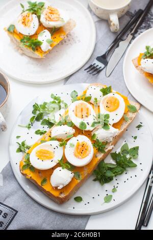 Geröstetes Brot mit Kürbismus, Frischkäse, grünen Zwiebeln, Kräutern und gekochten Eiern für gesundes Mittagessen oder Frühstück. Stockfoto