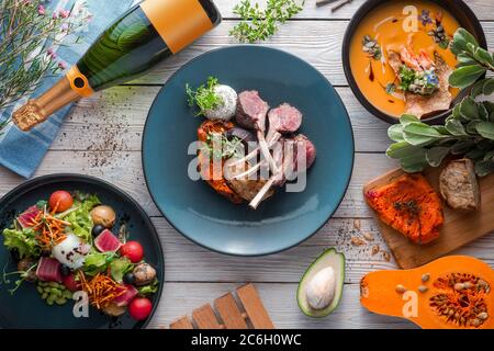 Saftiges Lammbrett mit Kürbis und Sahne-Kürbissuppe auf einem weißen Tisch. Restaurant serviert vom Koch. Holzhintergrund. Draufsicht. Flach liegend Stockfoto