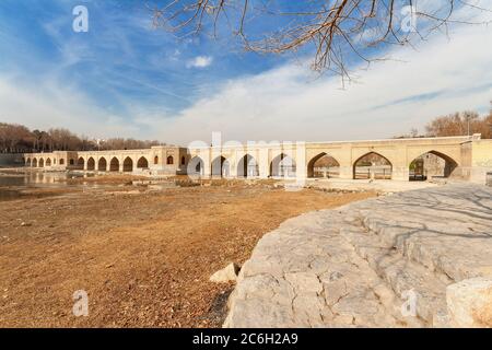 Der Blick auf die fast trockenen Flussbett des Zayandeh Fluss in Isfahan Stadt fließt, Central Iran. Strahlend blauen Himmel mit einigen Wolken über Chubi Brücke in wi Stockfoto