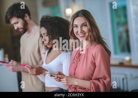 Lächelndes Mädchen in rosa Kleid, Freundin mit Freund Blick auf Smartphones Stockfoto