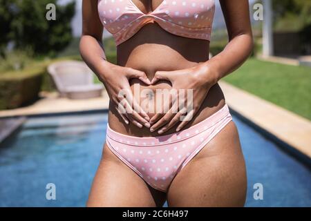 Mittlere Sektion der Frau, die ihre Hände in Herzform auf ihrem Bauch hält Stockfoto