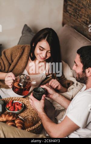 Ein glückliches Paar, das mit Croissants und Tee im Bett frühstückte Stockfoto