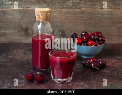 Frisch hausgemachter Kirschsaft im Glas und Flasche auf einem Holztisch mit reifen Beeren in einer Töpferschale. Stockfoto