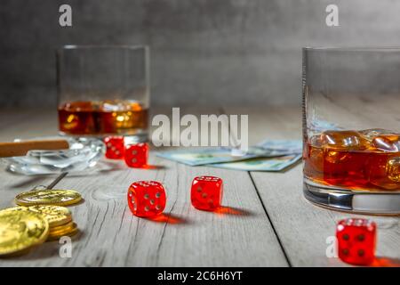 Rustikaler Holztisch. Zigarre in einem Aschenbecher und zwei Gläser Whiskey mit Eiswürfeln. Würfel und Dollarscheine. Wenige Bitcoin Stockfoto