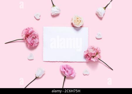 Urlaubskarte. Rosa Hintergrund mit weißem Papier in einer Mitte von Rosen umgeben. Stockfoto