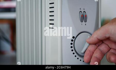 Man stellt die Heiztemperatur eines elektrischen Heizkörpers zu Hause in einem kalten Raum ein Stockfoto