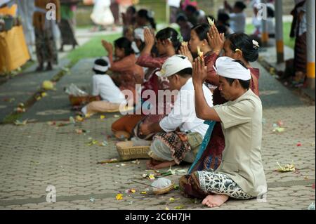 Männer mit Udeng-Kopfbedeckung und Menschen, die während des Siat Sampian Coconut Leaf war Festivals, Pura Samuan Tiga, Ubud, Bali, Indonesien, beten Stockfoto