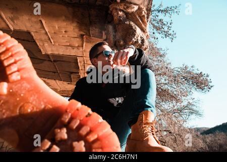 Attraktiver Kaukasischer, der an einem kalten Wintertag auf einer alten Wand sitzt und in die Ferne blickt. Tragen schwere wasserdichte Stiefel, eine in der für Stockfoto
