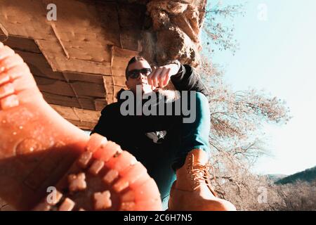 Attraktiver Kaukasischer, der an einem kalten Wintertag auf einer alten Wand sitzt und in die Kamera schaut. Tragen schwere wasserdichte Stiefel, eine in der Stirn Stockfoto