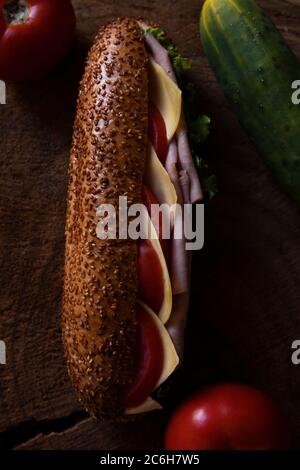 Sandwich mit Salami, Schinken, Salat, Scheiben von frischen Tomaten und Käse auf Holzoberfläche Stockfoto