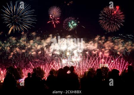 Mehrfaches Feuerwerk gegen einen schwarzen Himmel, Menschenmenge im Vordergrund Stockfoto