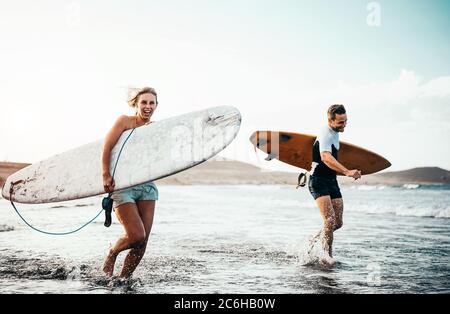 Surfer Paar, dass zusammen mit surfbrettern am Strand bei Sonnenuntergang - Sportliche Freunde Spaß zu surfen. Stockfoto