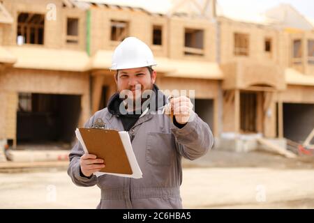 Kaukasischer Vorarbeiter, der Wohnungsschlüssel gibt und Zeichnungsplan in Notizbuch hält. Stockfoto