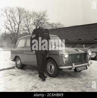 1960er Jahre, historisch, winterlich und mit Schnee auf dem Boden draußen, ein Sergeant der Royal Artillery in seiner Uniform für ein Foto von seinem Austin A40 Auto, England, Großbritannien. Das 1716 gegründete Royal Regiment of Artillery, bekannt als „The Gunners“, ist eines von zwei Regimentern, die den Artilleriearm der britischen Armee bilden. Stockfoto