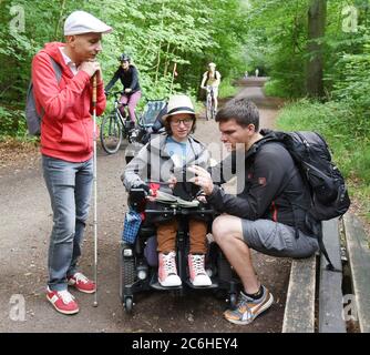 10. Juli 2020, Sachsen, Leipzig: Im Auenwald in Leipzig schauen die Kartographin Katharina Kohnen und Andre Neutag (r), Physiotherapeutin und Heilpädagogin mit Schwerpunkt Inklusion, vor einer viertägigen Wanderung von Leipzig nach Dresden Bilder auf einer Kamera an. Benny Tröllmich (l.), Berater des Vereins Leben mit Handicap, der selbst blind ist, begleitet sie auf den ersten zwölf Kilometern. Die 28-jährige Katharina, die aufgrund einer Muskelerkrankung auf einen elektrischen Rollstuhl angewiesen ist, und die 31-jährige Andre wollen auf Einschlussprobleme bei alltäglichen li hinweisen Stockfoto