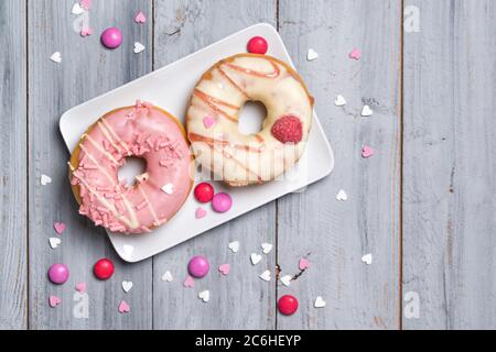 Zwei Donuts auf einem Teller mit Smarties und streut Herzen, Holzhintergrund dekoriert Stockfoto