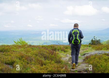 Mann, der vom Berg auf dem felsigen Weg geht. Der Typ in grauer Trainingskleidung und einem grünen Rucksack Stockfoto