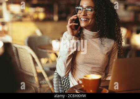 Schöne Frau, die am Telefon spricht und wegschaut. Frau, die im Café sitzt und telefoniert. Stockfoto