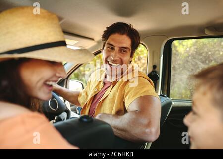 Familie, die im Auto Urlaub machen. Lächelnder Vater und Mutter drehen sich um zu ihrem Sohn, der auf dem Rücksitz des Autos sitzt. Stockfoto