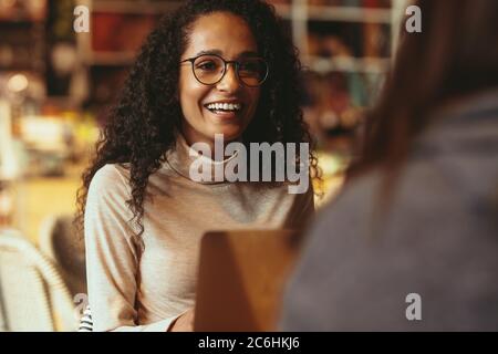 Lächelnde Frau, die im Café sitzt und mit einem Freund spricht. Frau, die ihre Freundin in einem Café trifft. Stockfoto