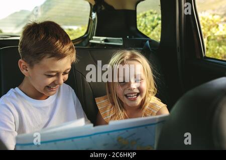 Zwei Kinder erkunden auf ihrer Fahrt mit dem Auto eine Karte. Kinder, die mit ihren Eltern in Urlaub gehen. Stockfoto