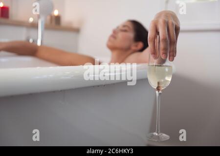 Frau hält ein Weinglas und entspannt sich in der Badewanne Stockfoto