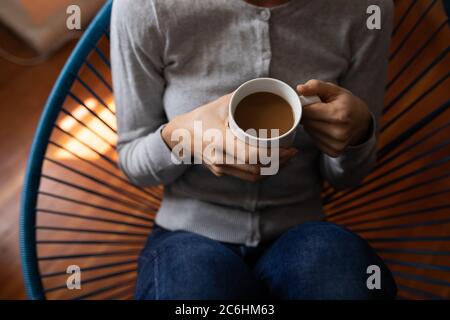 Mittlere Abteilung der Frau hält Kaffeetasse auf einem Stuhl sitzen Stockfoto