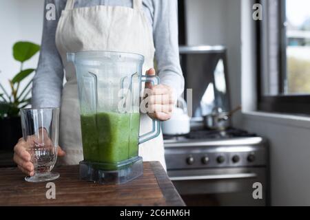 Mittlere Abteilung der Frau in Schürze hält Glas und Glas Smoothie Stockfoto