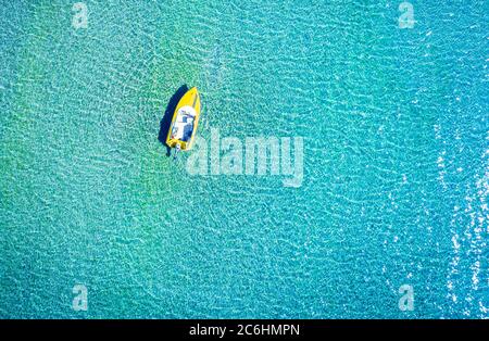 Luftaufnahme eines gelben einsamen Tboots, das in kristallklarem türkisfarbenem Meerwasser gefesselt ist
