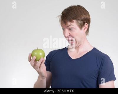 Portrait des jungen Mannes, der angewidert aussagt, während er Apfel hält Stockfoto