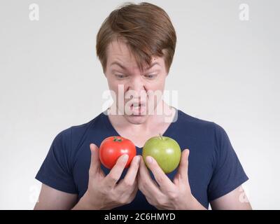 Portrait des jungen Mannes, der angewidert aussieht, während er Tomaten und Apfel hält Stockfoto