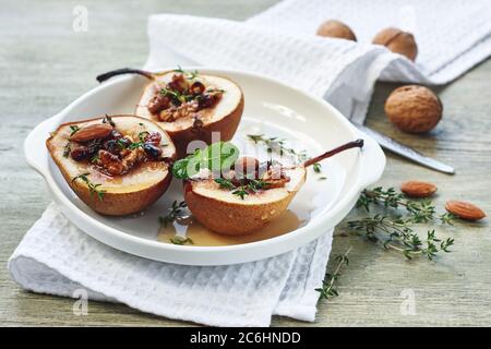 Gebackene Birnen mit Nüssen, Rosinen, Honig und Zimt auf einem weißen Teller auf einem grünen Holztisch. Stockfoto