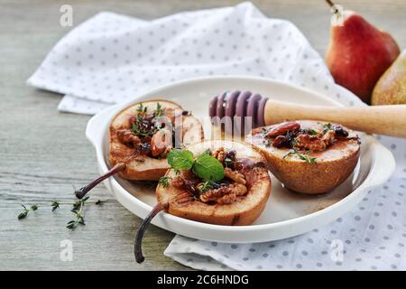 Gebackene Birnen mit Nüssen, Rosinen, Honig und Zimt auf einem weißen Teller auf einem grünen Holztisch. Stockfoto