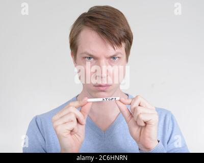 Porträt eines jungen Mannes, der ernst aussieht, während er die Zigarette mit STOPPSCHILD hält Stockfoto