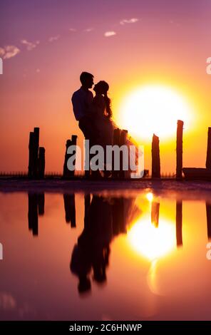 Silhouette der Brautpaare auf dem Hintergrund von Sonnenuntergang, Himmel, Säulen und deren Spiegelung im Wasser. Stockfoto