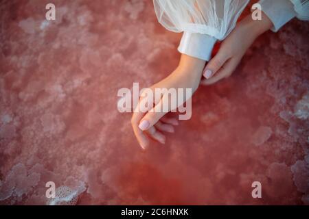 Frau streicht ihre Hände in den rosa salzigen Genichesk See mit Salzkristallen in der Ukraine. Nahaufnahme. Stockfoto