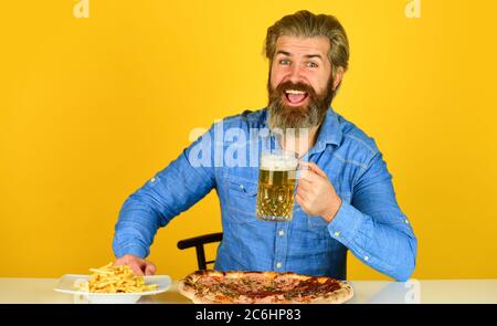 Glücklicher bärtiger Mann mit Bier und Pizza. italienisches Essen. Pommes Frites. Mann in der Bar Bier Glas trinken und Pizza essen. Cheers. Fußball im Fernsehen. american Fast Food. Stockfoto