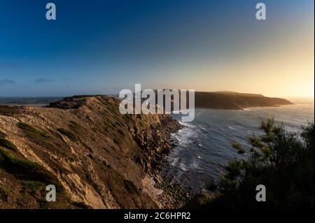 Blick auf die Landzungen am Eingang der Bucht São Martinho do Porto, mit dem Leuchtturm, bei Sonnenuntergang. Stockfoto