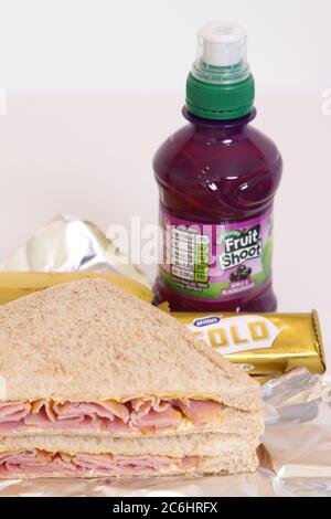 Inhalt der Lunchbox in einer britischen Schule. Schinken-Senf-Sandwich mit Goldschokolade und Obstschrot. Stockfoto