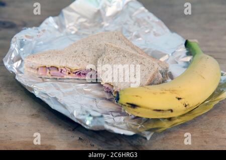 Halb gegegessen Schinken Sandwich mit Banane, verpackt Mittagessen in Folie Stockfoto
