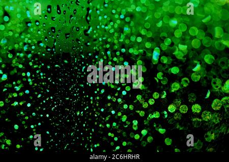 Wassertropfen durch ein Fenster. Glühende grüne Partikel. Stockfoto