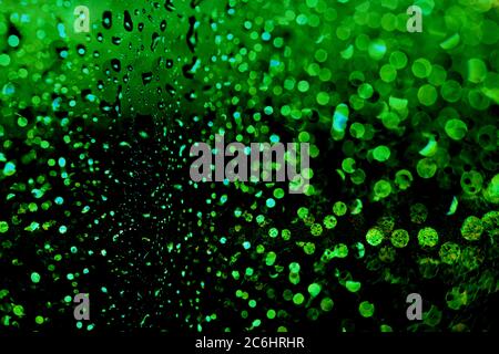 Wassertropfen durch ein Fenster. Glühende grüne Partikel. Stockfoto