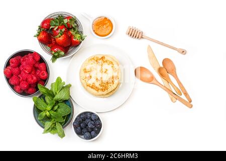 Pfannkuchen auf einem Teller und Beeren in Schüsseln auf weißem Hintergrund Stockfoto