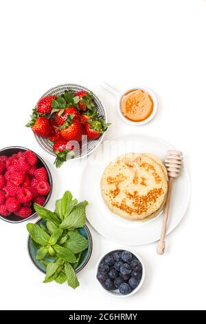 Pfannkuchen auf einem Teller und Beeren in Schüsseln auf weißem Hintergrund Stockfoto